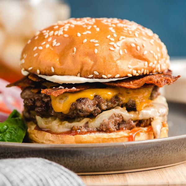 A double cheeseburger with bacon, melted cheese, and sauce on a sesame seed bun.