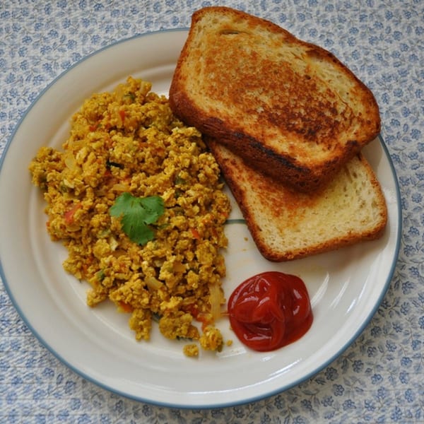 Scrambled eggs with vegetables, two slices of toast, and a dollop of ketchup on a white plate.
