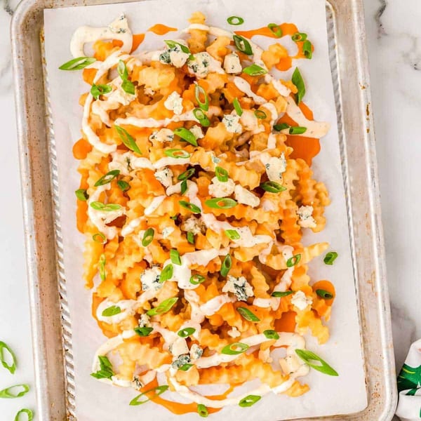 Buffalo chicken fries with blue cheese crumbles, ranch, and green onions on a baking sheet.